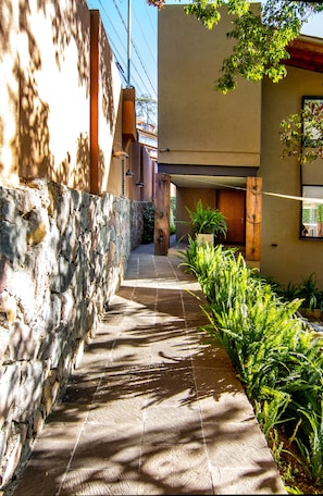 A narrow stone pathway flanked by a stone wall and a building with a wooden door and a window.