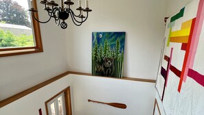 Une pièce décorée d’un tableau représentant un ours et des arbres, avec un mur orné d’une batte de baseball et une fenêtre donnant sur un paysage verdoyant.