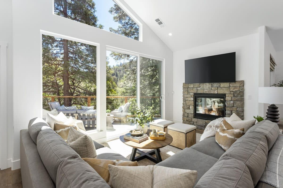 A modern living room with a stone fireplace, a large flat-screen TV, and a sofa set.