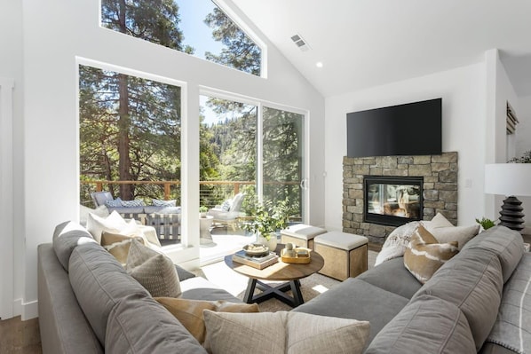 A modern living room with a stone fireplace, a large flat-screen TV, and a sofa set.