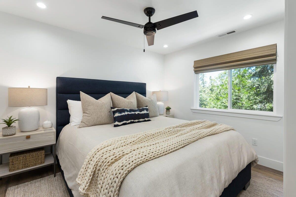 Une chambre à coucher comprenant un lit, des tables de chevet, un ventilateur de plafond, une fenêtre avec vue et une lampe de chevet.