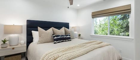 Un dormitorio con cama, mesitas de noche, ventilador de techo, ventana con vistas y lámpara de noche.