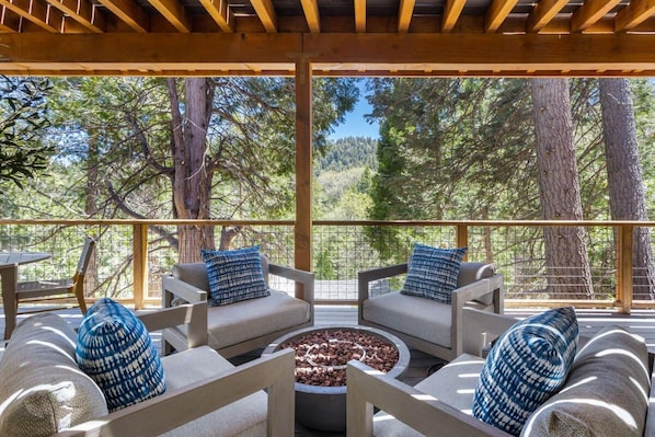 An outdoor seating area with a fire pit, surrounded by wooden furniture and blue patterned cushions.