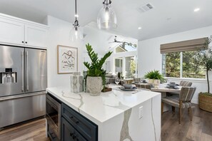 A modern kitchen with a central island, stainless steel appliances, pendant lighting, and a dining area with a view.
