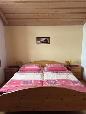 A double bed with a patterned bedspread, wooden headboard, two bedside tables with lamps, and a framed picture on the wall.