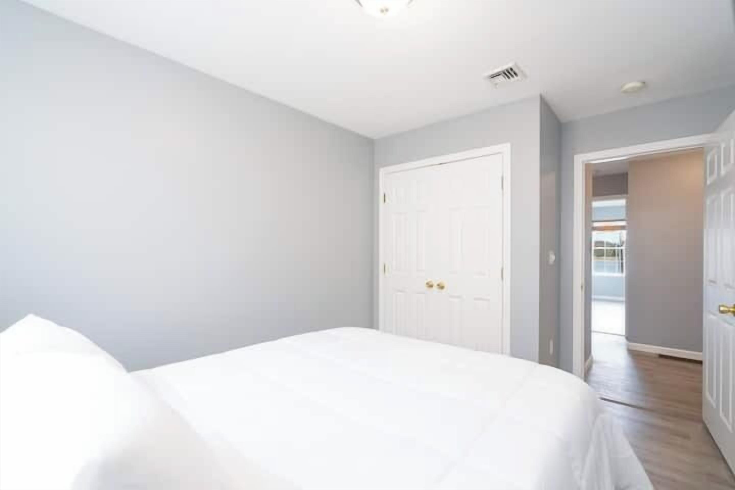 A bedroom with a bed, a white door, and a hallway leading to a balcony.