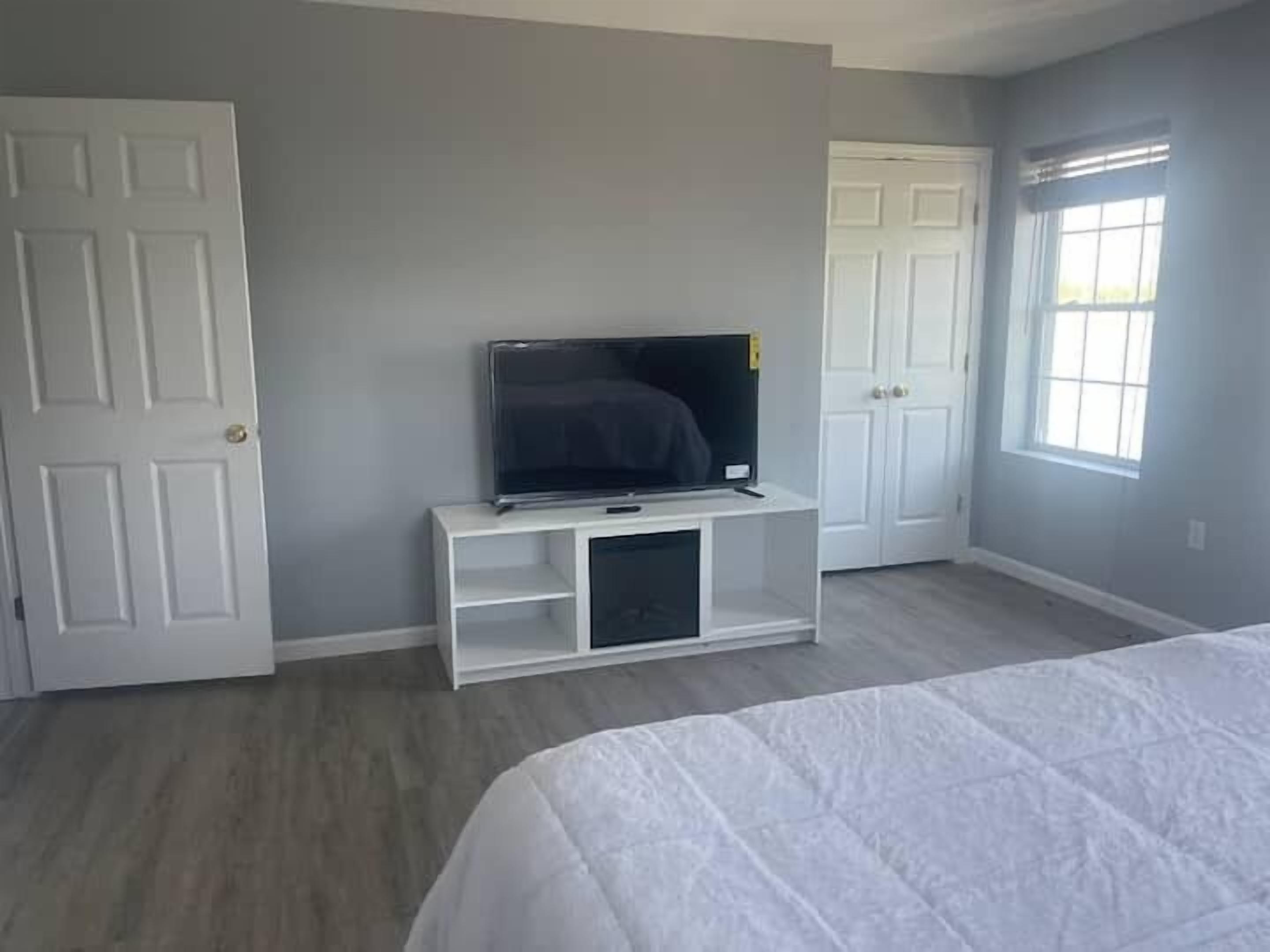 Un dormitorio con una cama, un televisor sobre un mueble, una puerta y una ventana.