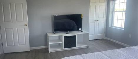 Un dormitorio con una cama, un televisor sobre un mueble, una puerta y una ventana.