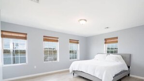 A spacious bedroom with a large bed, three windows with blinds, and a light-colored wooden floor. - Gorgeous Waterfront 3 Bedroom, 1.5 Bathroom Unit. (New Haven)