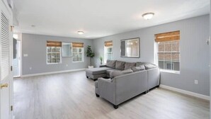 A spacious living room with a grey sectional sofa, a small ottoman, and a large window with a view. - Gorgeous Waterfront 3 Bedroom, 1.5 Bathroom Unit. (New Haven)