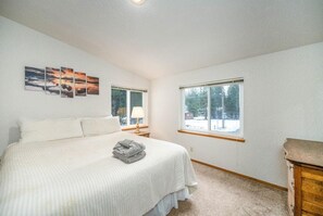 Un dormitorio con cama, mesita de noche, lámpara, cómoda y ventana con vista a árboles.