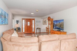 Una sala de estar con un sofá beige, un mueble de madera, un televisor y una puerta que da a otra habitación.