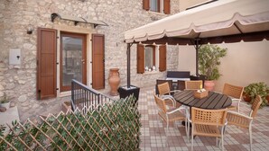 Un bâtiment en pierre doté d’un patio comprenant une table ronde, des chaises et un grand parasol.