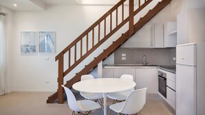 Une cuisine moderne avec des meubles blancs, un escalier en bois et un coin repas comprenant une table et des chaises blanches.