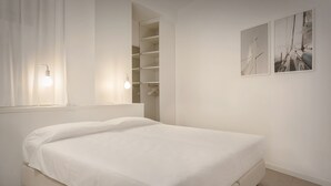 Une chambre à coucher au style minimaliste, comprenant un lit, un dressing et deux appliques murales.