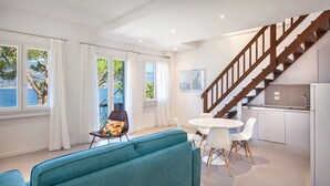 Un salon moderne avec un canapé de couleur turquoise, une table à manger avec des chaises blanches, un escalier et un coin cuisine.
