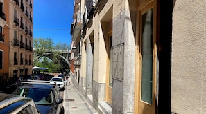 A narrow street with parked cars and a building with a large window and a door marked "Studio entrance."