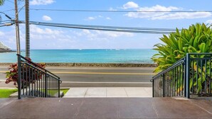 A view from a balcony overlooking a beach with a clear sky and calm sea. - Summer Deal Downtown Kona Vacation Condo Walk to Shops Dining and Beach (Kailua Kona)