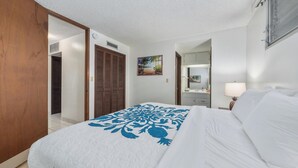 A hotel room with a bed, a wooden wardrobe, a painting, a bathroom with a mirror, and a window. - Summer Deal Downtown Kona Vacation Condo Walk to Shops Dining and Beach (Kailua Kona)