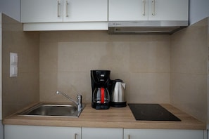A compact kitchen with a sink, a coffee maker, a kettle, and a black induction cooktop.