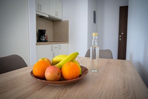 A dining table with a fruit bowl containing apples and oranges, a glass of water, and a bottle of water.