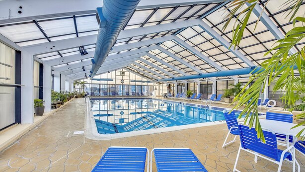 An indoor swimming pool with blue lounge chairs and a covered area with a glass ceiling. - DAILY ACTIVITIES & LINENS INCLUDED*! CAPRI - 3BR Direct Oceanfront Updated Condo! (Ocean City)