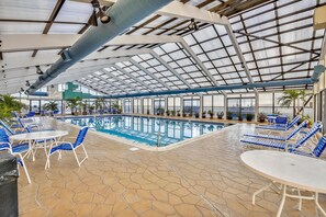 Une piscine intérieure avec des chaises longues et des tables bleues, entourée de plantes en pot.