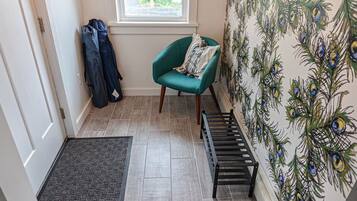 A room with a teal armchair, a window, a peacock-themed wallpaper, a wooden floor, and a black metal bench.
