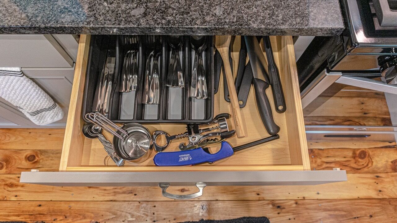Un cajón con diversos utensilios de cocina, incluyendo cucharas, cuchillos y una herramienta con mango azul.