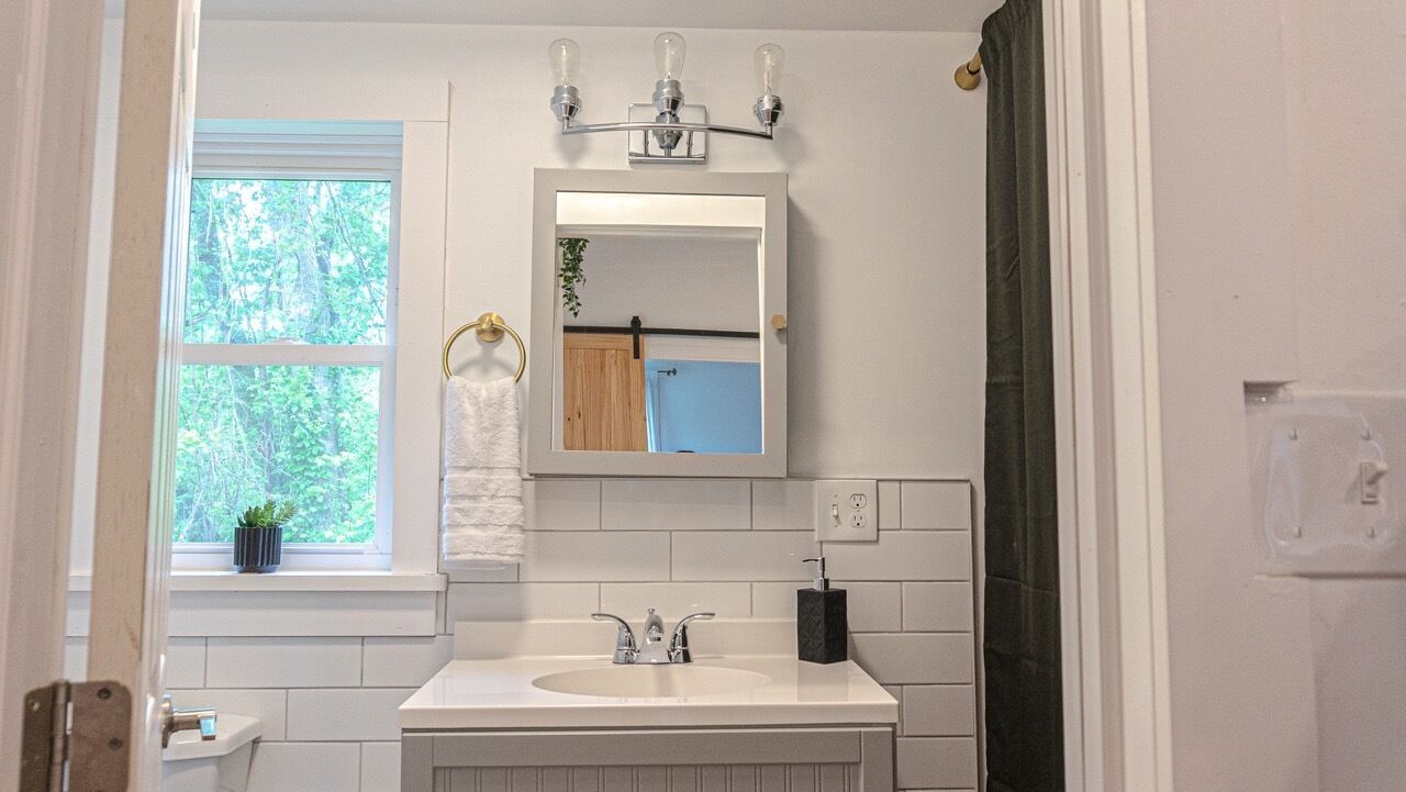 A bathroom with a white sink, a mirror, and a window with a view of trees.