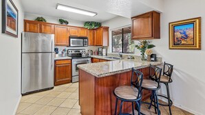 A kitchen with wooden cabinets, stainless steel appliances, a granite countertop, and a bar area with stools. - Sedona Condo, Close to Dining/Shopping/Hiking (Sedona)