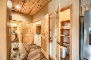 A hallway with wooden doors, a washing machine, a refrigerator, and a table with a decorative item. - OM A9 Gruene Mill Inn at Old Mills Resort (New Braunfels)
