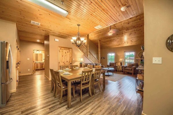 A spacious kitchen with wooden flooring, a dining area with a wooden table and chairs, a staircase, and a living area with a sofa and a coffee table.