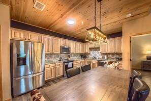 A modern kitchen with wooden cabinets, stainless steel appliances, and a large dining table.