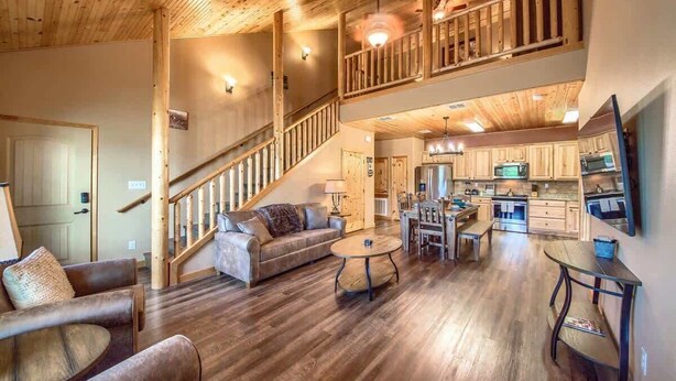 A spacious living area with a wooden staircase, a kitchen with modern appliances, and a dining area with a round table. - OM A8 Gruene River Two-Step at Old Mills Resort (New Braunfels)