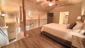 Un dormitorio con techo de madera, una cama, una mesita de noche, un televisor y una escalera.