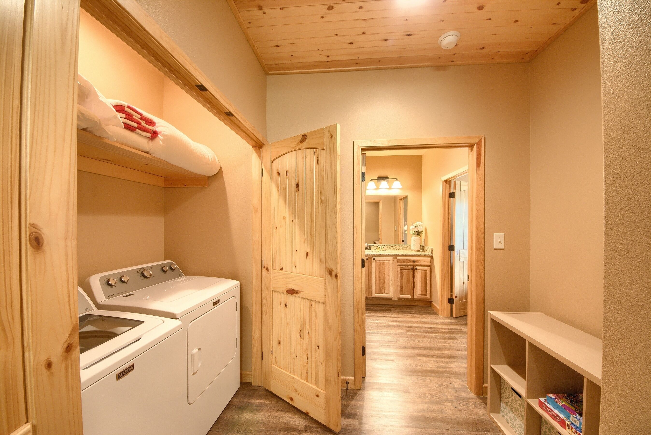 A laundry room with a washing machine and dryer, wooden door, and a hallway leading to a bathroom with a sink and mirror.
