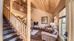 A spacious living area with a wooden staircase, a comfortable sofa, a television, and a large mirror.