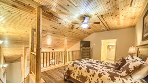 A bedroom with a wooden ceiling, a bed with a cowhide-patterned bedspread, a ceiling fan, and a TV on a dresser. - Old Mills Resort OM A6 3 Bedroom Condo by RedAwning (New Braunfels)