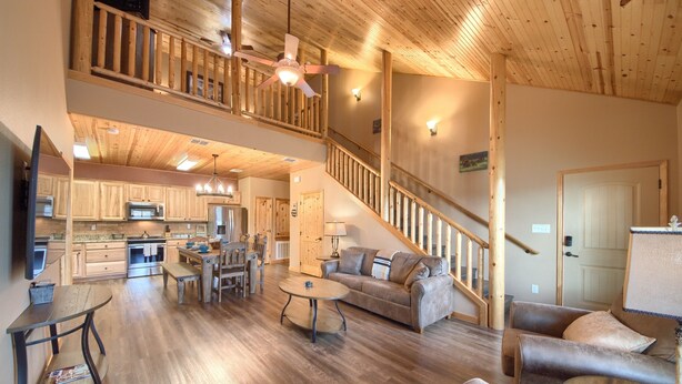 A spacious living area with a wooden ceiling, a staircase, and a kitchen in the background. - Old Mills Resort OM A6 3 Bedroom Condo by RedAwning (New Braunfels)