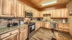 Une cuisine dotée de meubles en bois, de plans de travail en granit, d’appareils électroménagers en acier inoxydable et d’un plafond en bois.
