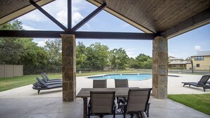 Une terrasse extérieure avec une piscine, des piliers en pierre et un espace salon abrité.