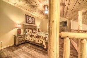 A bedroom with a wooden ceiling, a bed with a cowhide blanket, two bedside lamps, and a framed picture on the wall. - Old Mills Resort OM A8 3 Bedroom Condo by RedAwning (New Braunfels)
