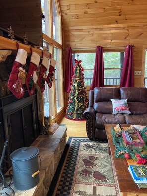 Un salon chaleureux avec une cheminée, un sapin de Noël, un canapé en cuir et des décorations festives.