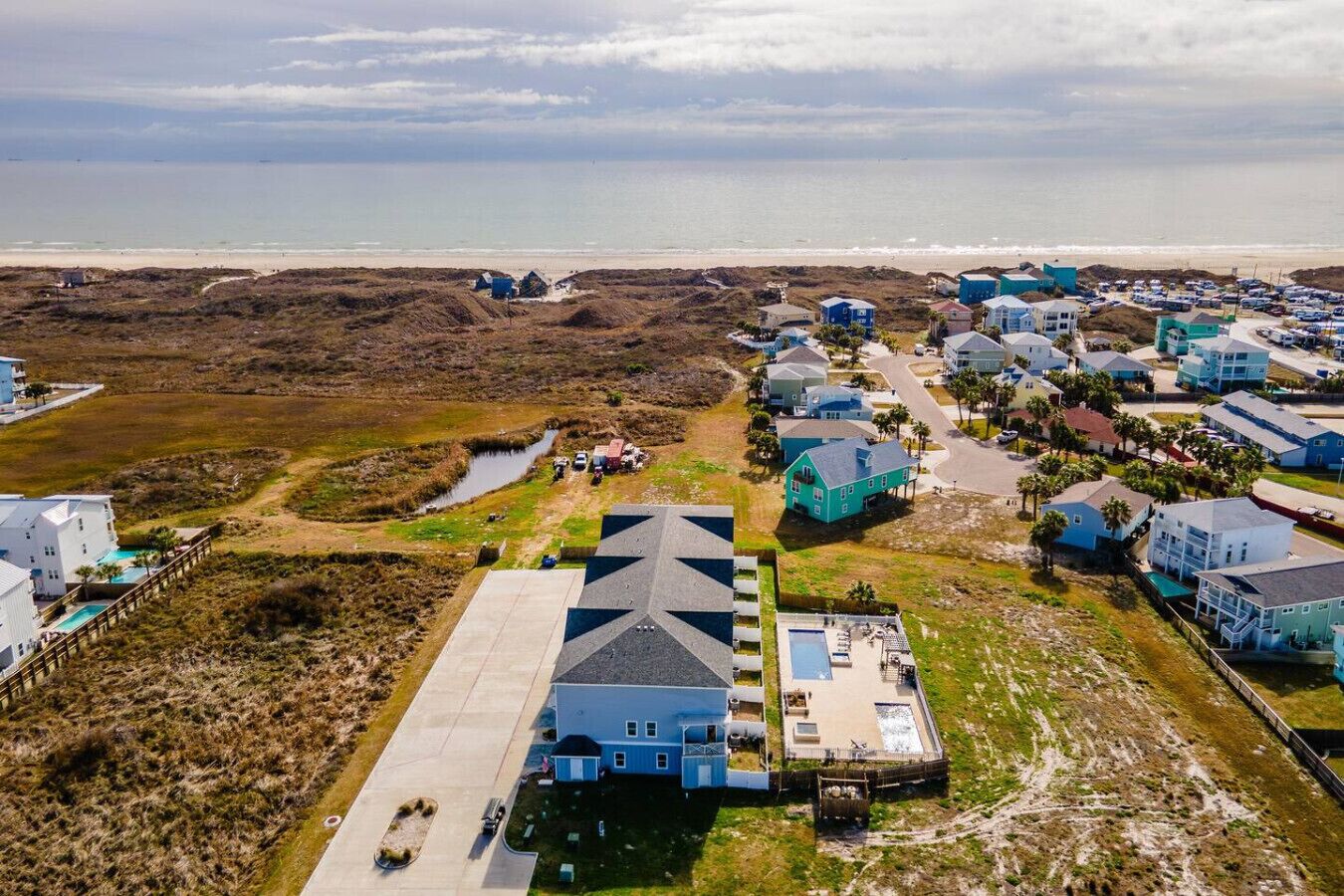 Un quartier résidentiel situé sur la côte, avec des maisons, un grand immeuble doté d’une piscine et une plage en arrière-plan.