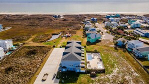 A coastal residential area with houses, a large building with a pool, and a beach in the background. - Dive In and Unwind: Pet-Friendly Living with Community Pools and Hot Tubs. (Port Aransas)