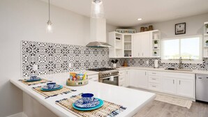 A modern kitchen with white cabinets, a central island, patterned backsplash, and pendant lighting. - Dive In and Unwind: Pet-Friendly Living with Community Pools and Hot Tubs. (Port Aransas)