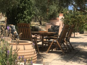 An outdoor seating area with a round table and wooden chairs, surrounded by greenery and a stone wall. - Private Two-house Villa With Pool in Olive Garden (Archanes-Asterousia)