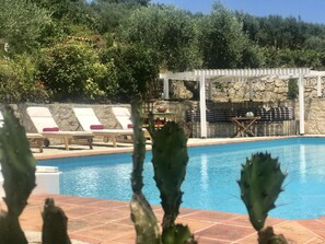 A pool area with lounge chairs, a pergola, and a stone wall. - Private Two-house Villa With Pool in Olive Garden (Archanes-Asterousia)