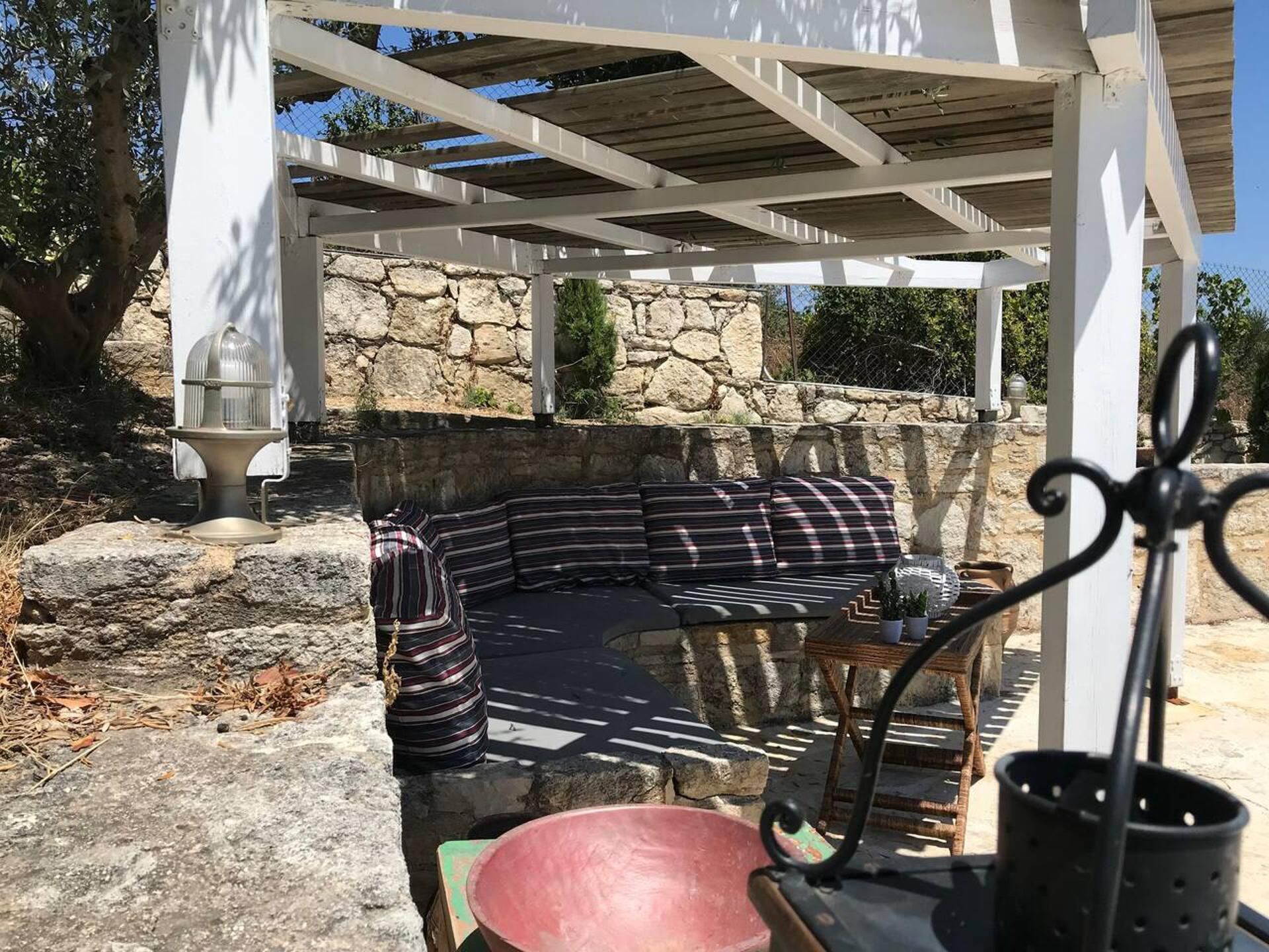 Uma área de estar coberta ao ar livre com um painel de parede de pedra, uma churrasqueira de metal e uma cesta trançada.